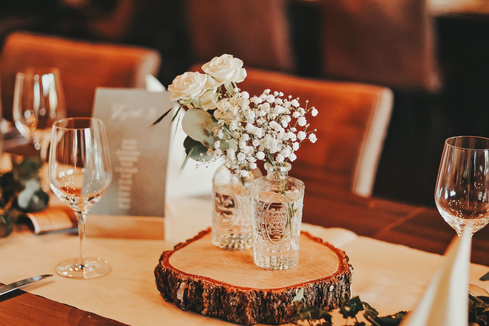 Weiße Rosen und Schleierkraut in Vintage-Glasflaschen auf einer Holzscheibe