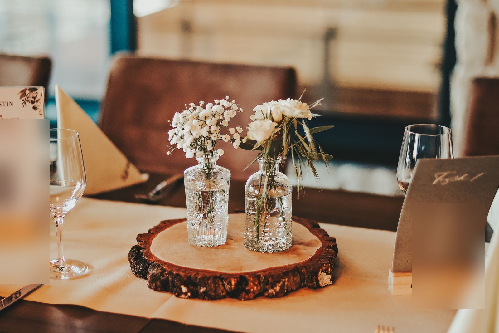 Zwei Vintage-Glasfläschchen mit Schleierkraut und Rosen auf einer Baumscheibe