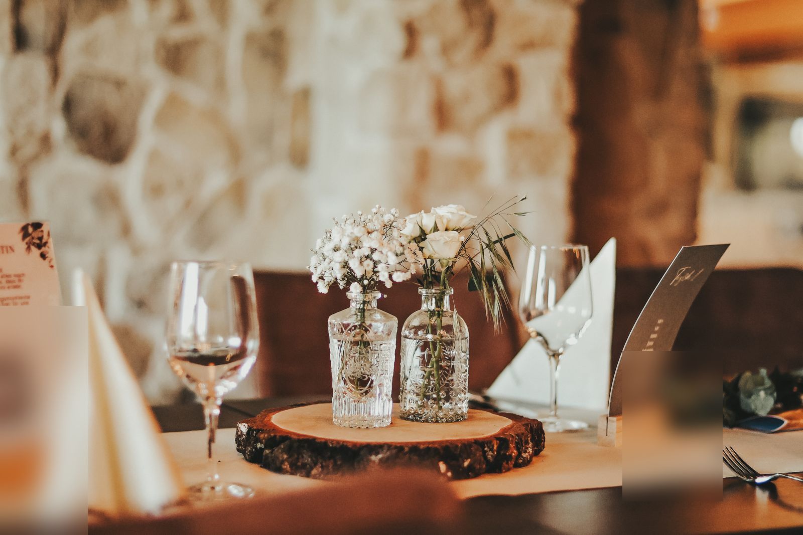 Hochzeitstisch mit Weinglas, Kerze und Blumendeko auf Baumscheibe vor Steinwand