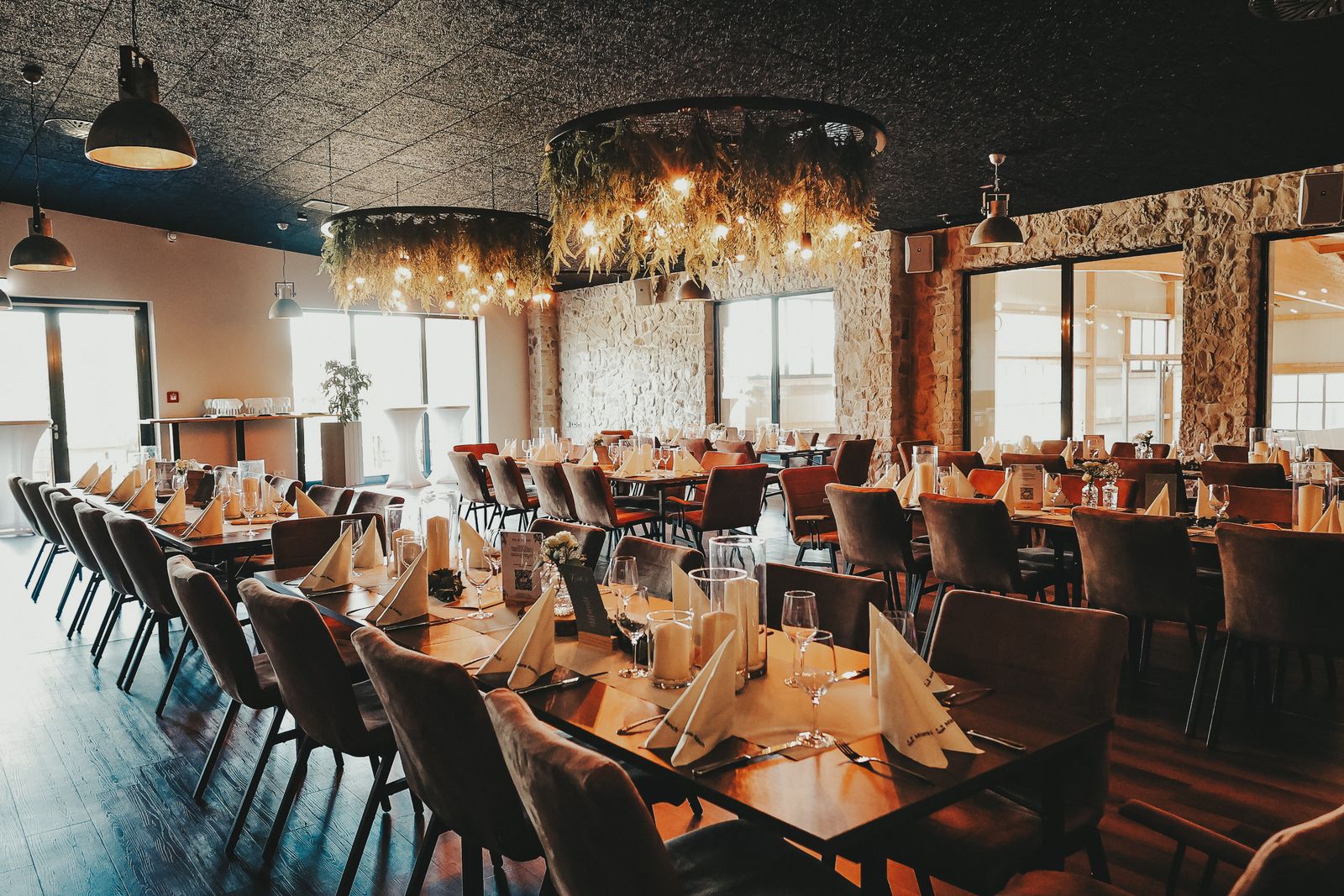 Festsaal mit eingedeckten Hochzeitstischen, Natursteinwand und Lichterkranz